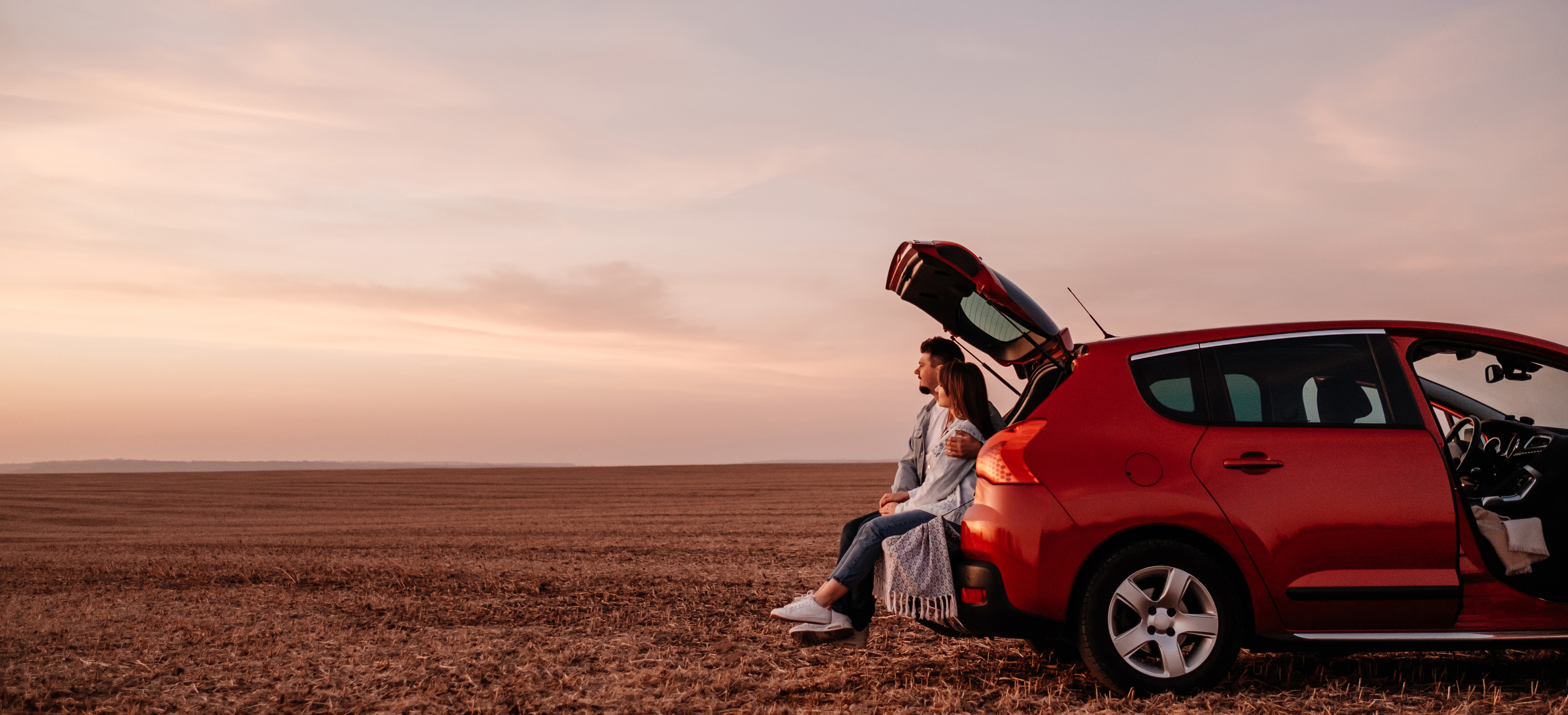 Photo of couple sitting in their car looking at sunset. 